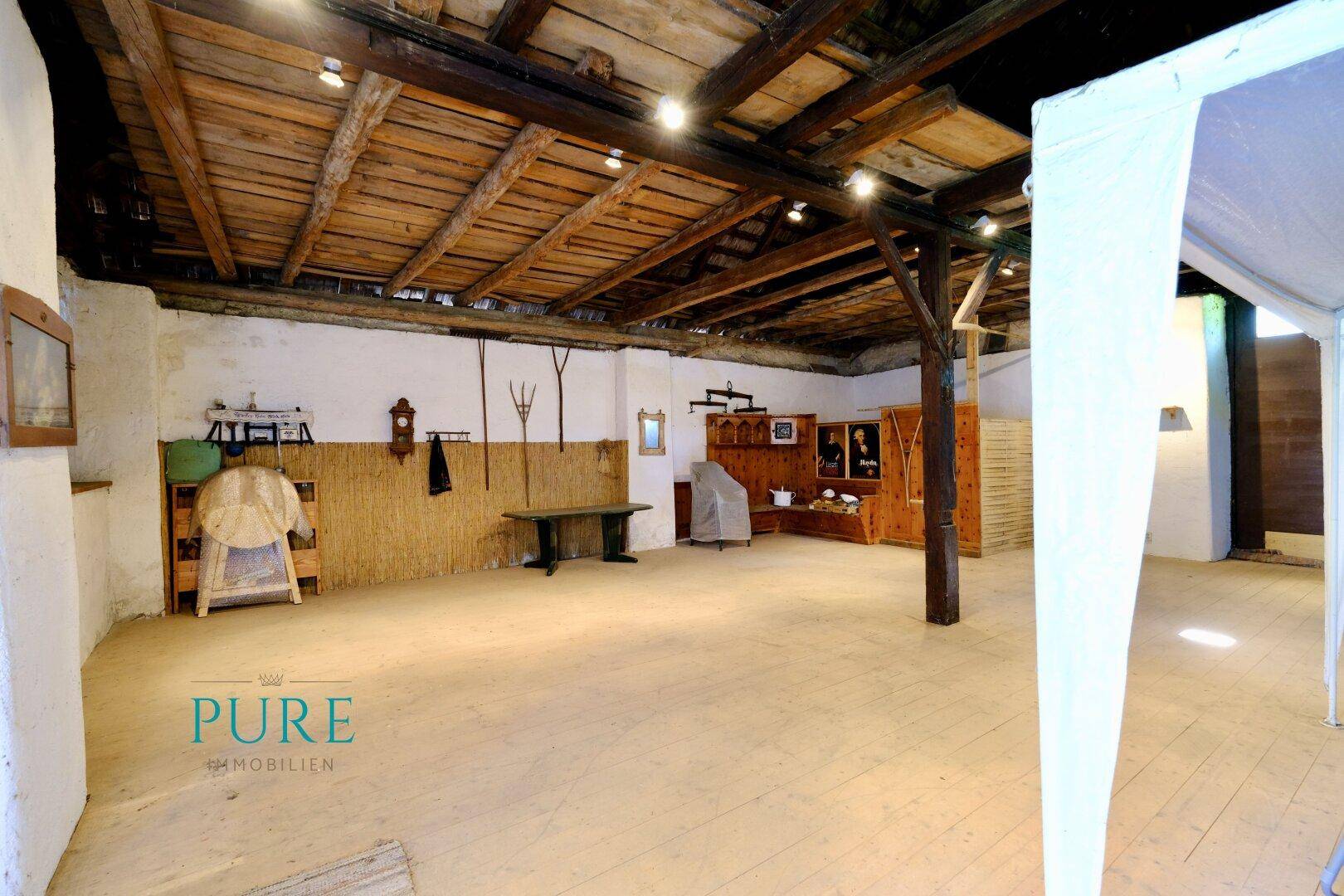 Rustikaler Innenraum mit sichtbaren Holzbalken und Dielenboden, möglicherweise ein umgebauter Scheunenbereich.