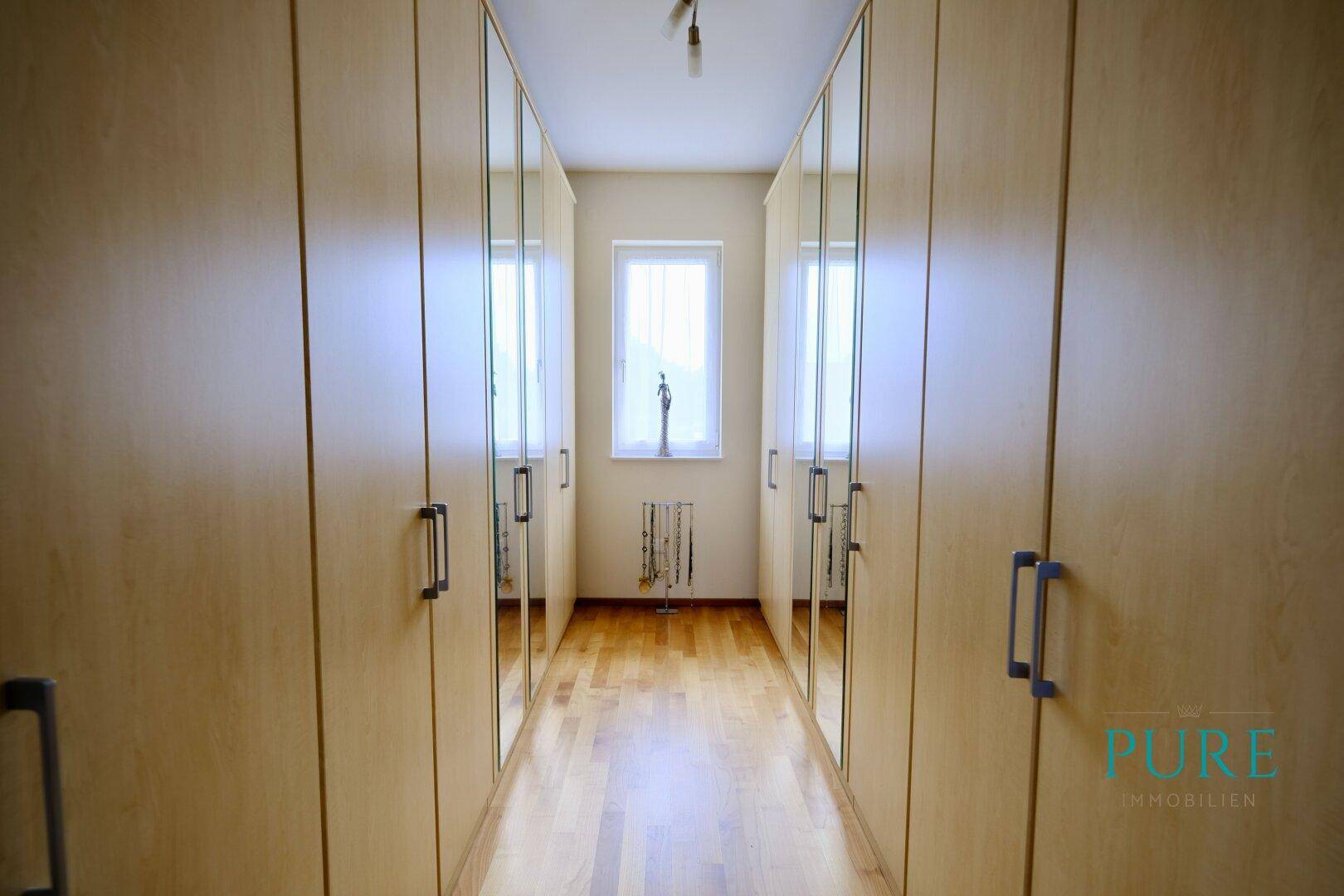 Heller Ankleideraum mit Einbauschränken, Spiegeltüren und Holzfußboden.