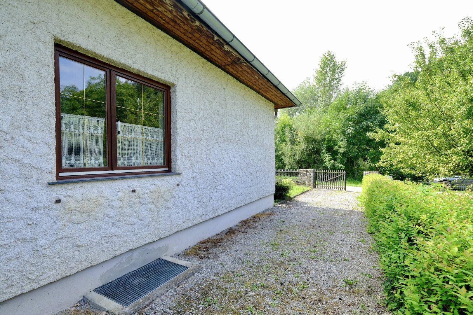 Seitenansicht des Hauses mit Fenster, Kiesauffahrt und gepflegter Hecke.