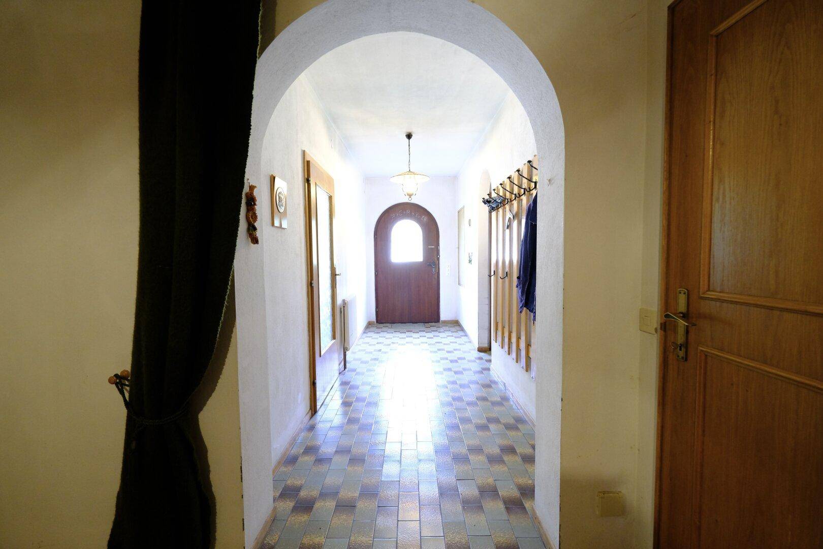 Heller Eingangsbereich mit traditionellem Fliesenboden, Rundbogen und Garderobe.