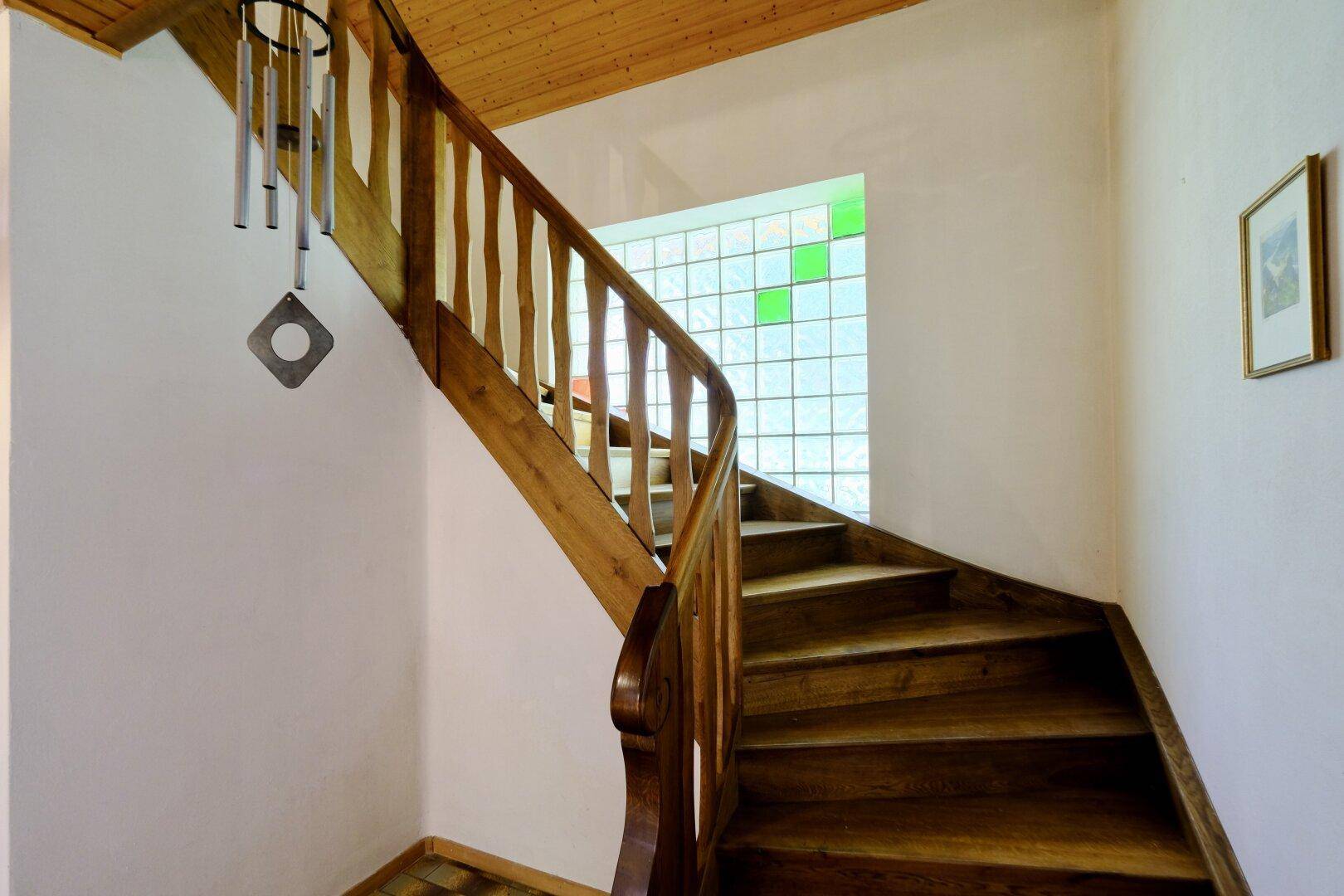 Holztreppe mit geschnitztem Geländer und einem farbigen Glasbausteinfenster.