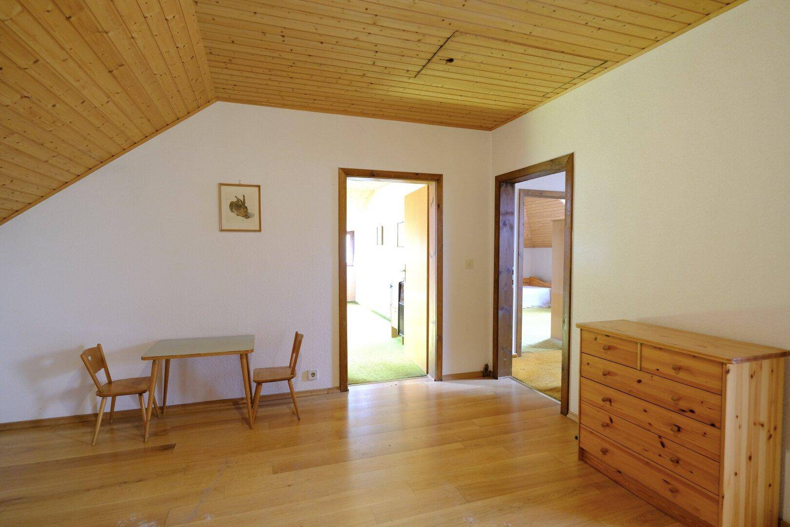Dachgeschosszimmer mit Holzfußboden, Dachschräge und sichtbarer Holzdecke.