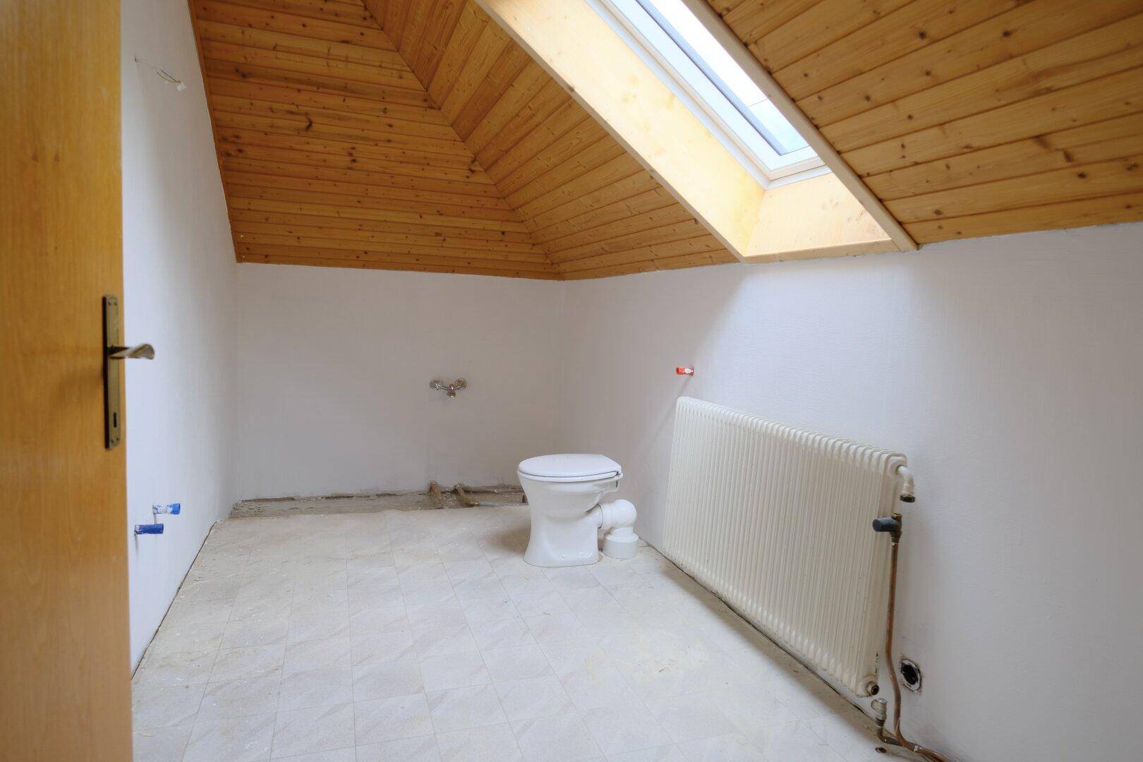 Unfertiges Badezimmer im Dachgeschoss mit Dachfenster, Toilette und Heizkörper.