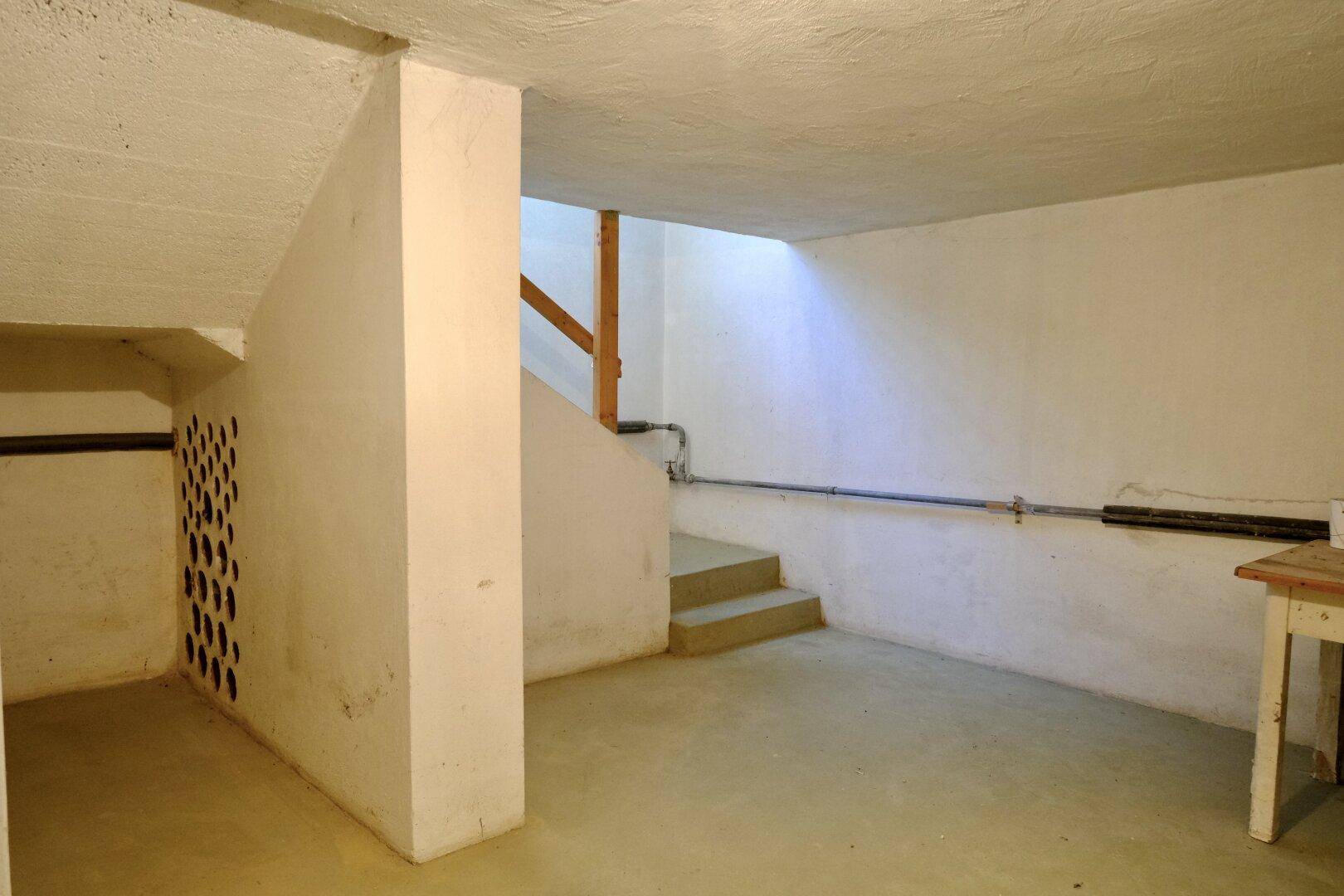 Geräumiger, unfertiger Kellerraum mit Betonboden und Treppenzugang.
