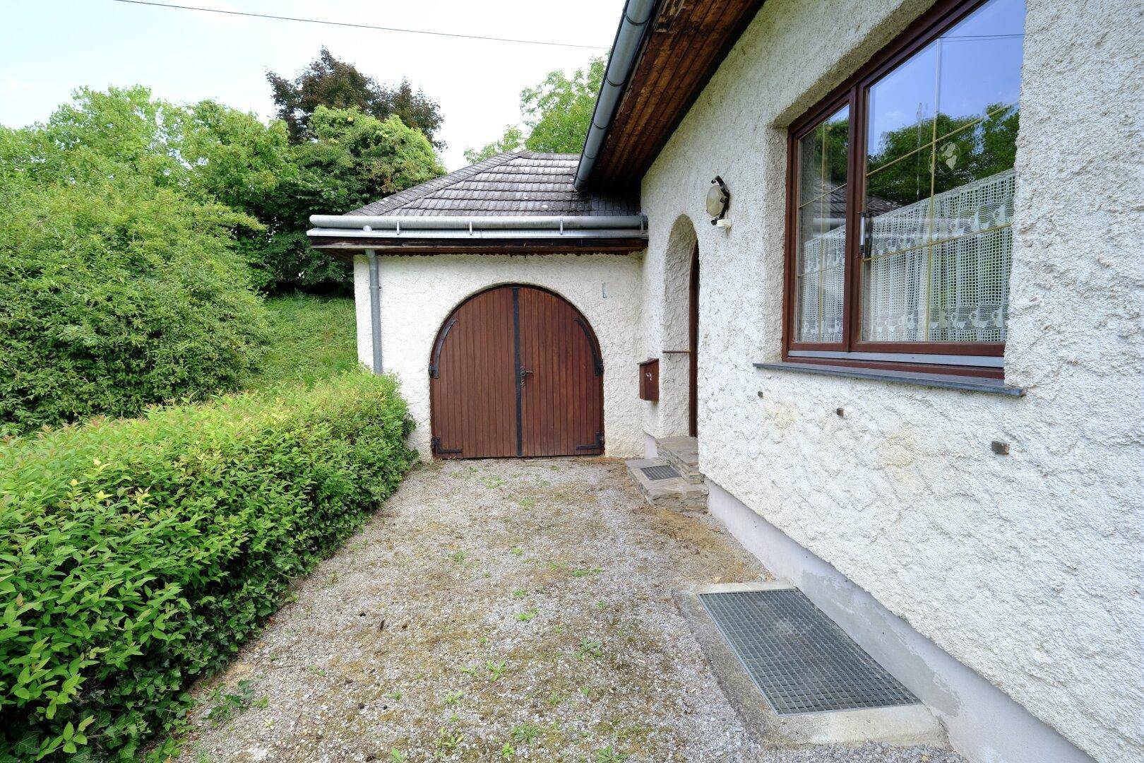 Außenansicht des Hauses mit Rundbogen-Garagentor, Kiesauffahrt und Hecke.