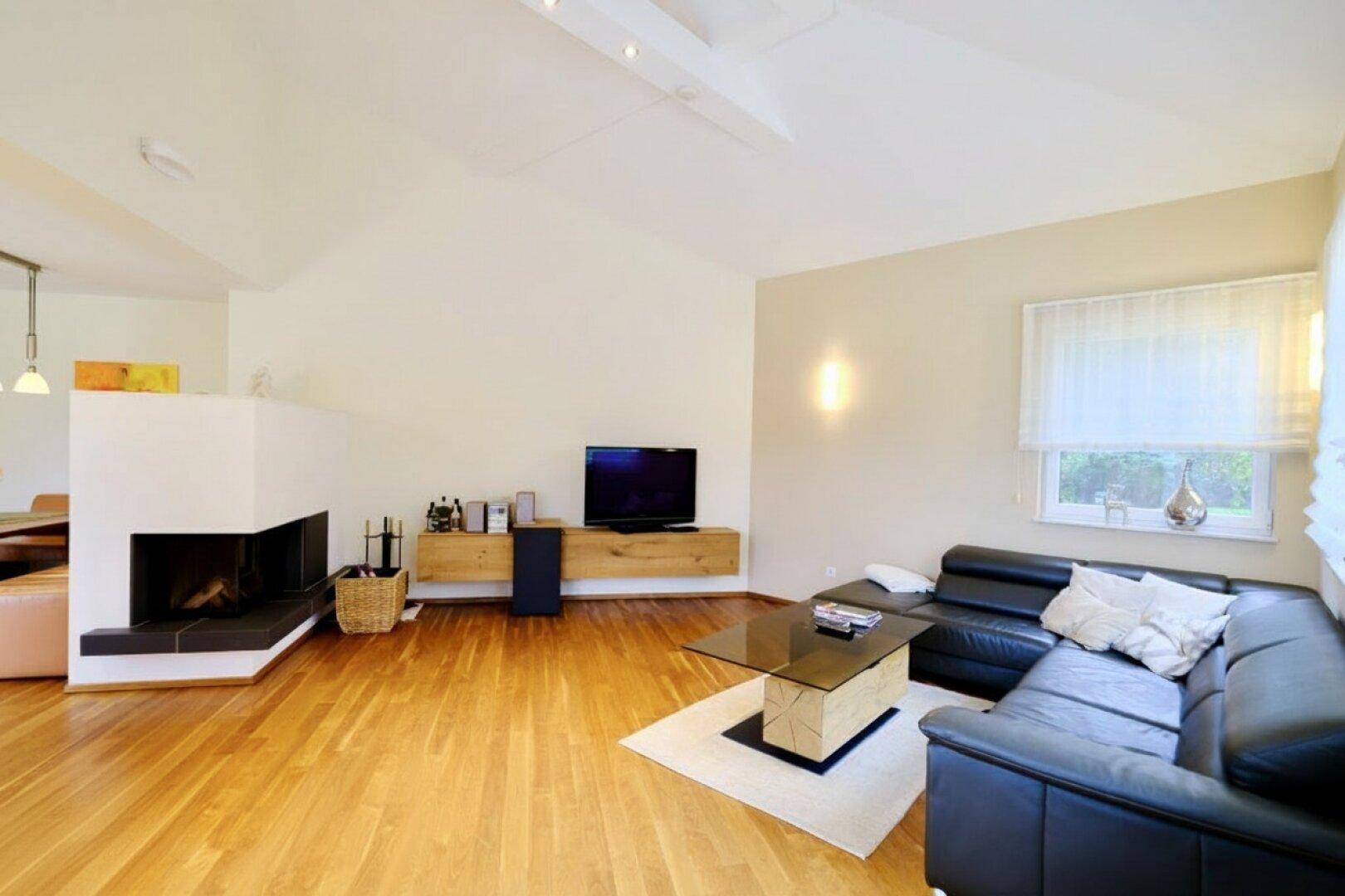 Gemütliches Wohnzimmer mit Kamin, dunklem Ledersofa und Holzboden, ideal zum Entspannen.