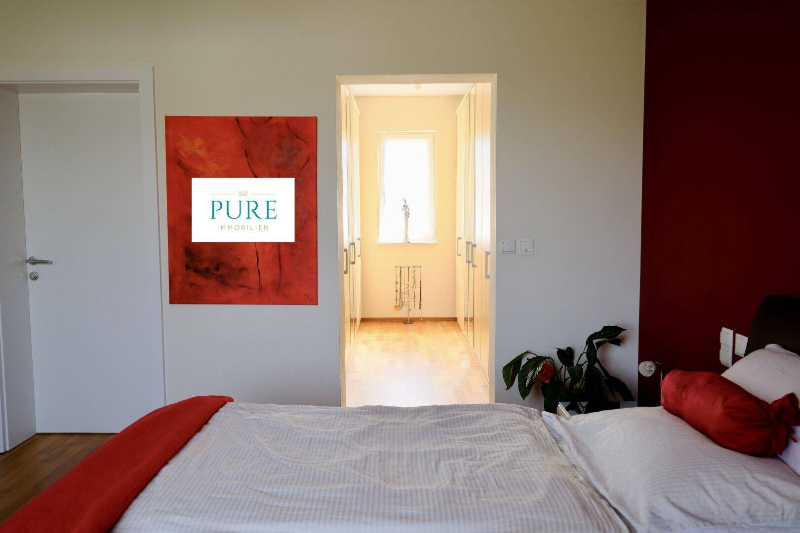 Schlafzimmer mit roter Akzentwand und Zugang zu einem begehbaren Kleiderschrank.