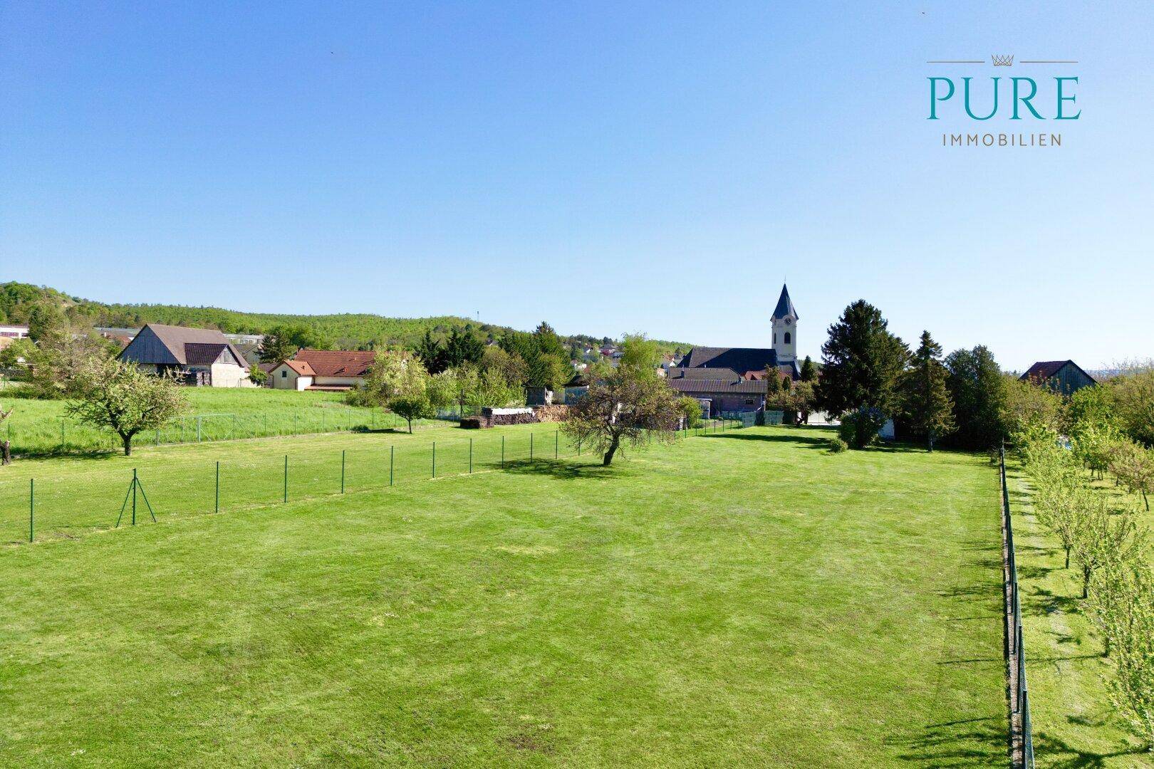 Weitläufige Grünfläche mit Obstbäumen und Blick auf die umliegende Landschaft und ein Dorf.
