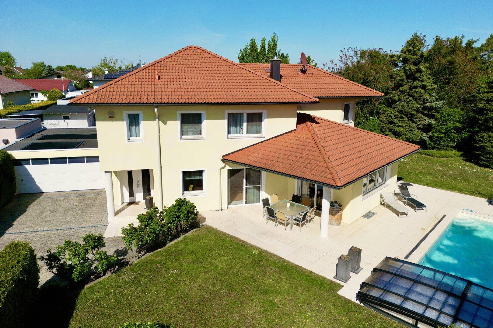 Großzügiges Einfamilienhaus mit Pool, Garage und weitläufigem Garten unter blauem Himmel.
