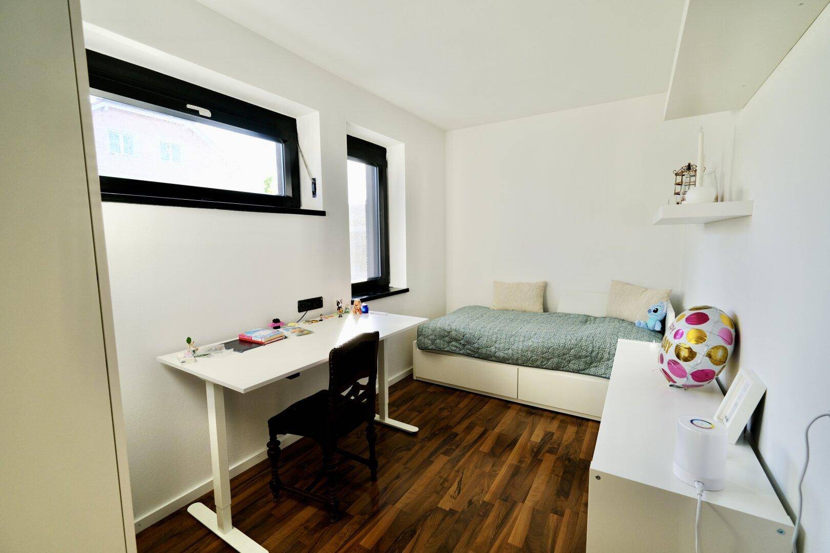 Helles Schlafzimmer mit Holzboden, Schreibtisch und Einzelbett, ideal als Kinder- oder Gästezimmer.