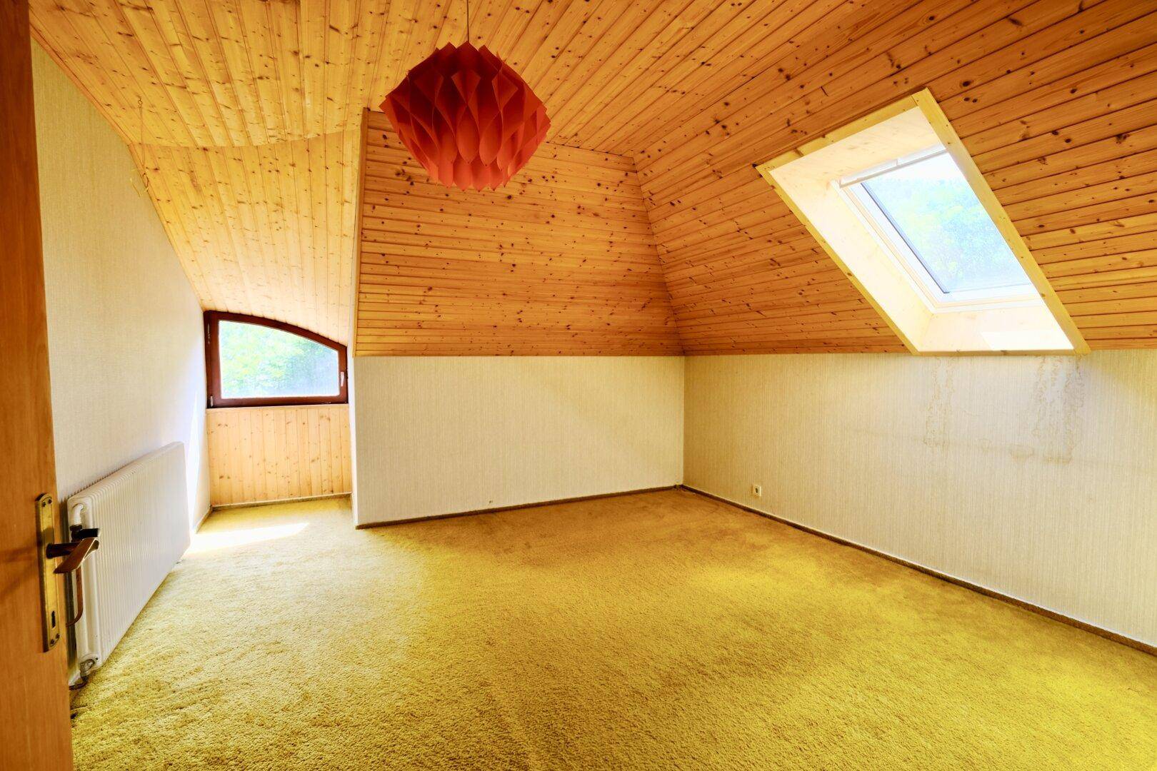 Helles Dachzimmer mit Holzverkleidung, gelbem Teppichboden und großem Dachfenster.