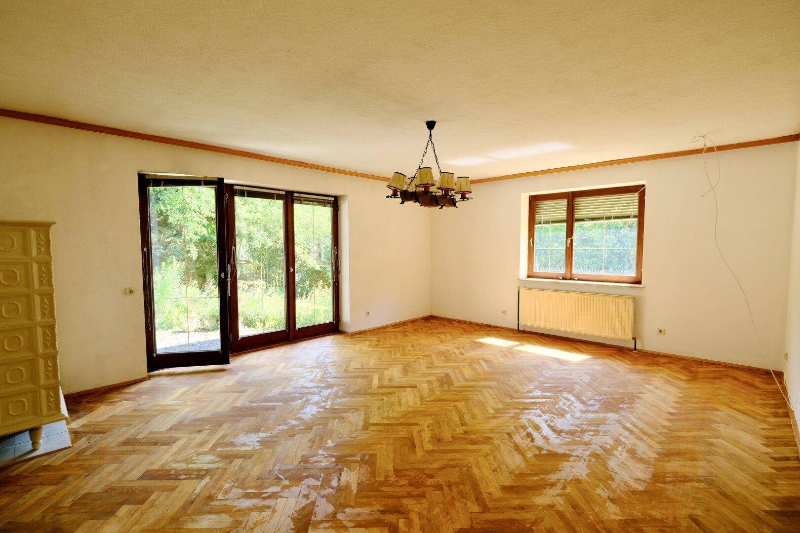 Helles Wohnzimmer mit Fischgrätparkett, Kachelofen und großen Fenstertüren zum Garten.