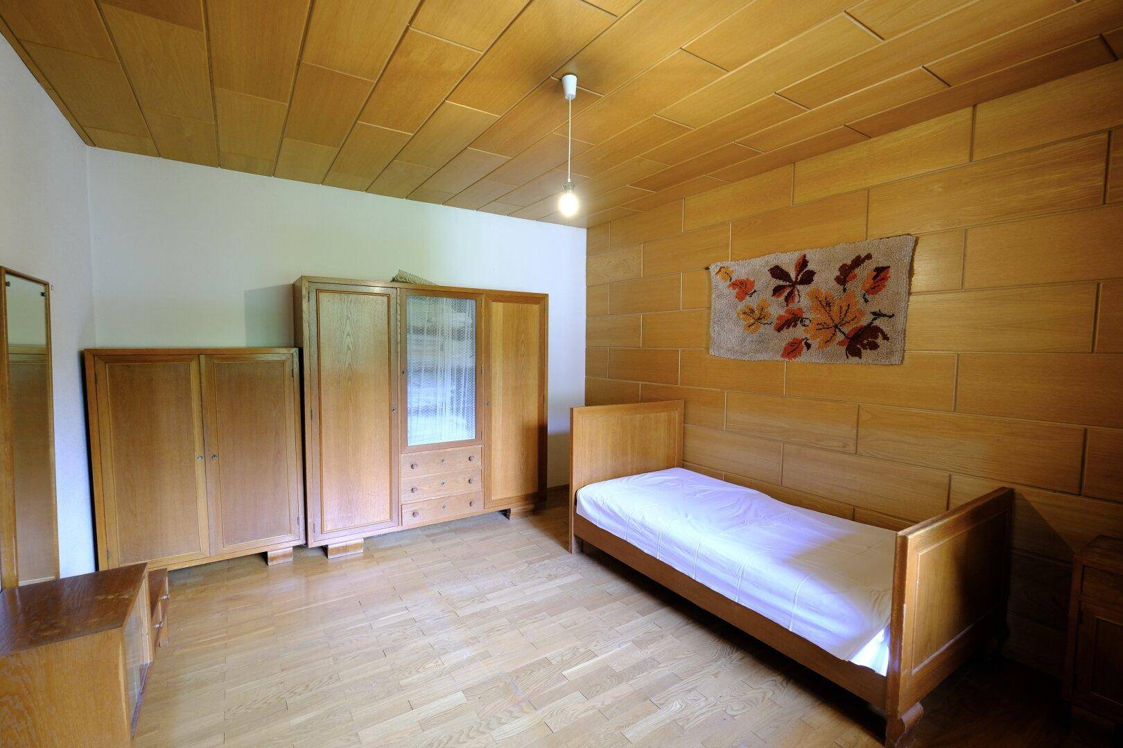 Schlafzimmer im Landhausstil mit Holzvertäfelung, Einzelbett und passenden Holzschränken.