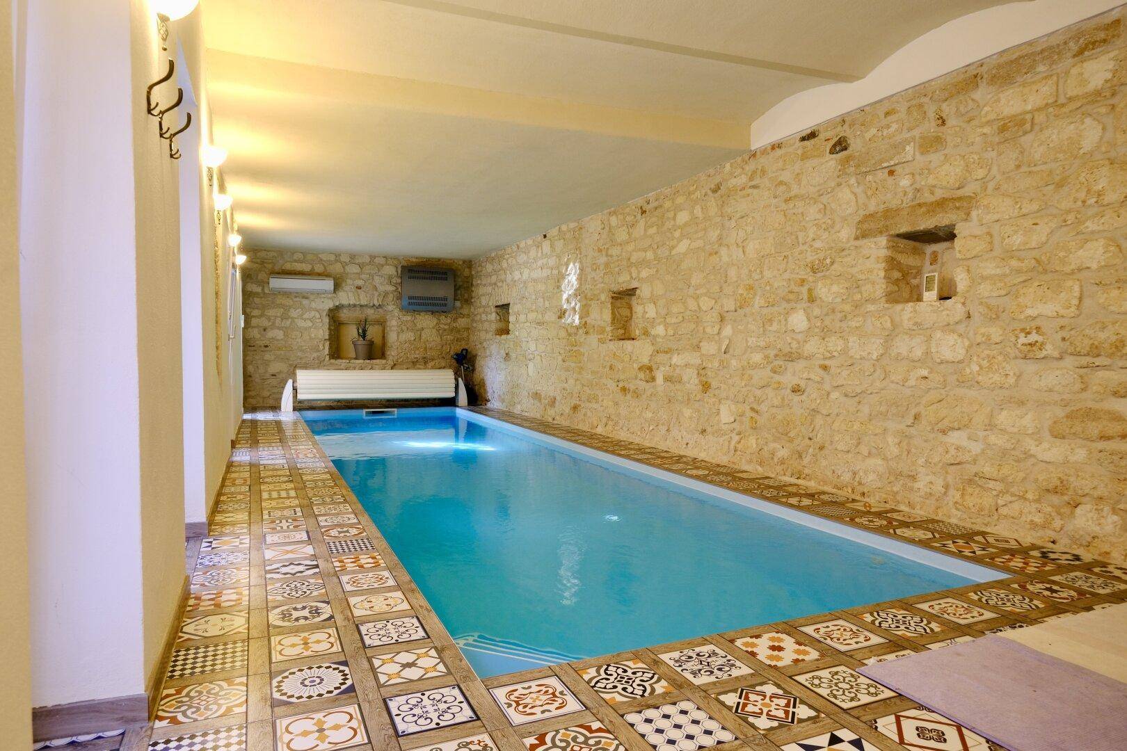 Innenpoolbereich mit Natursteinwänden und dekorativen Fliesen, ideal für Wellness.