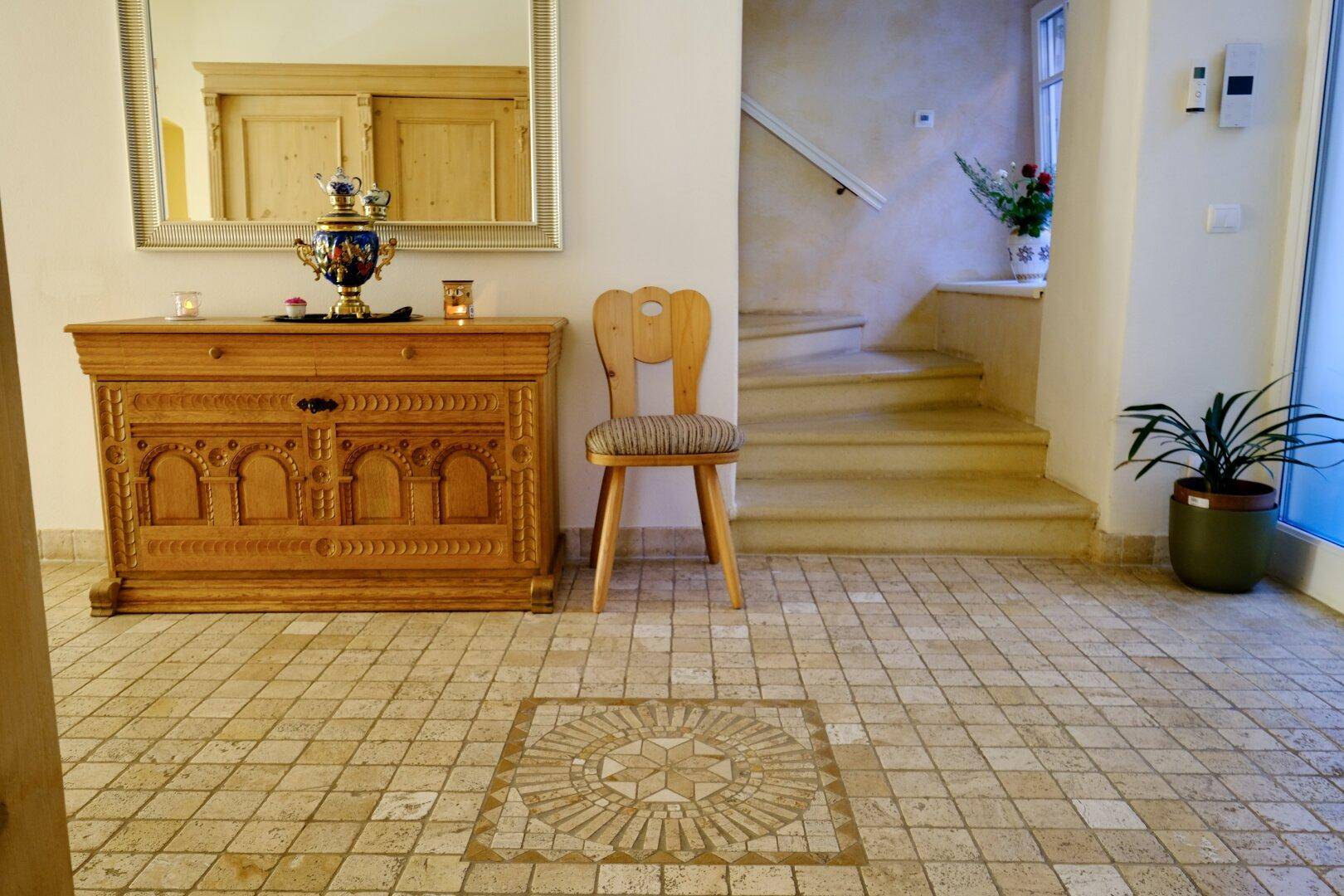 Detailansicht des Flurs mit Holztruhe, Stuhl und kunstvollen Bodenfliesenmuster.
