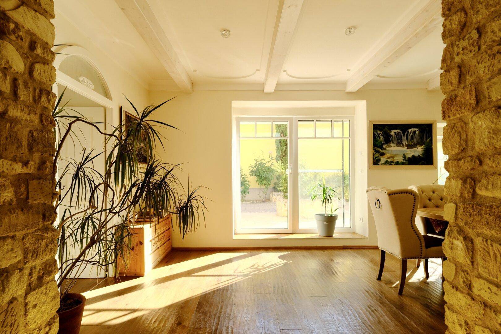 Lichtdurchfluteter Wohnbereich mit Holzboden, großen Fenstern und Blick in den Garten.