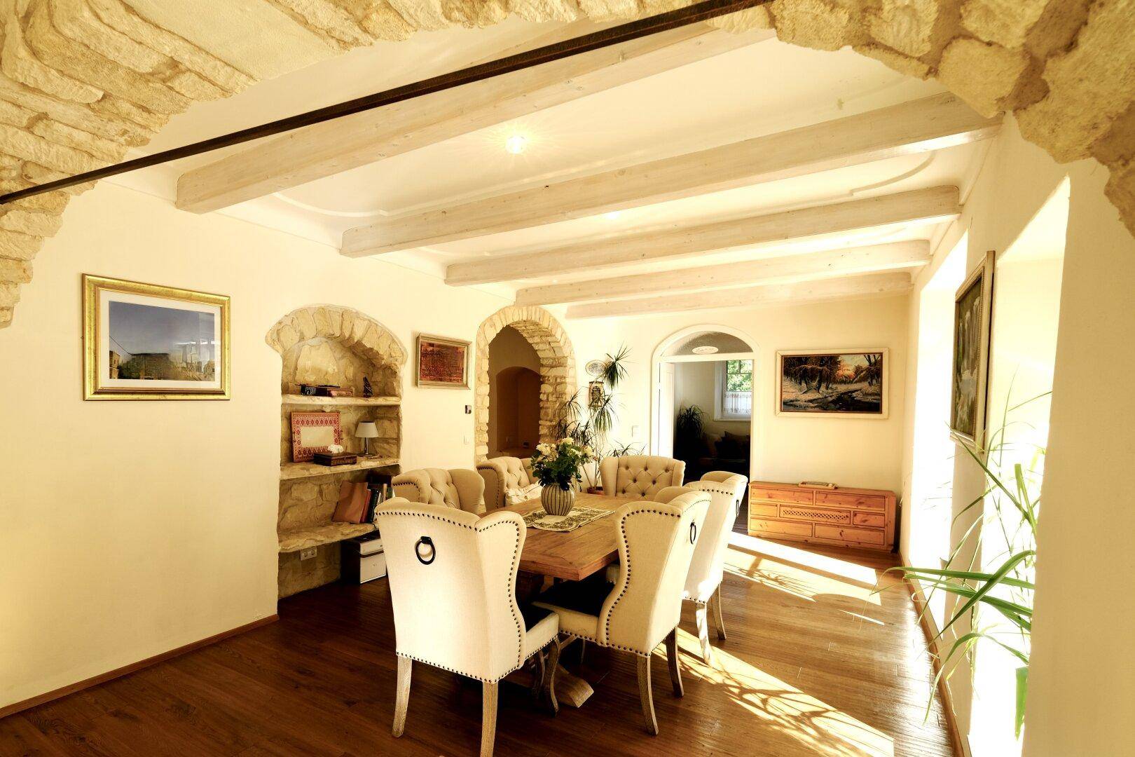 Eleganter Essbereich mit Holzboden, gepolsterten Stühlen und dekorativen Steinbögen.