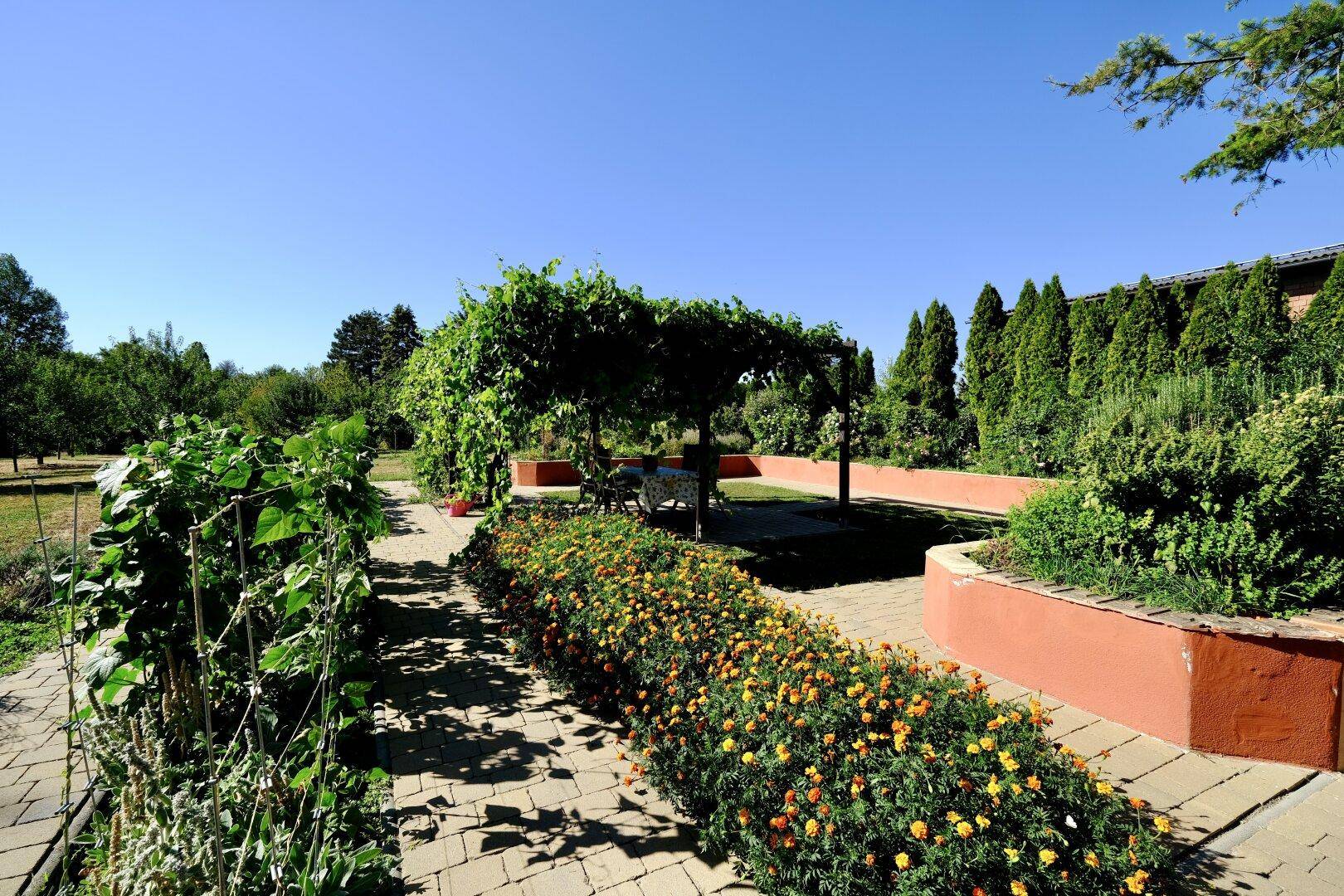Weitläufiger Garten mit Küchengarten, Blumenbeeten und einer Pergola im Hintergrund.