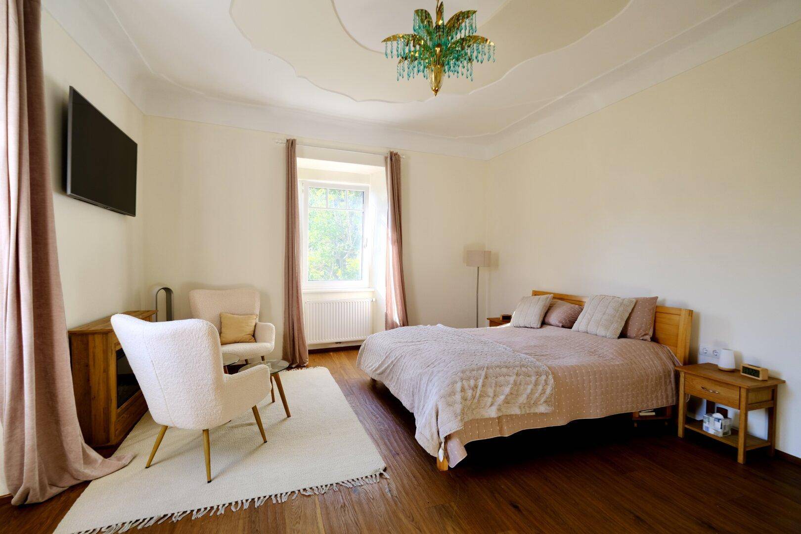 Geräumiges Schlafzimmer mit Holzboden, Doppelbett und eleganter Deckenleuchte.