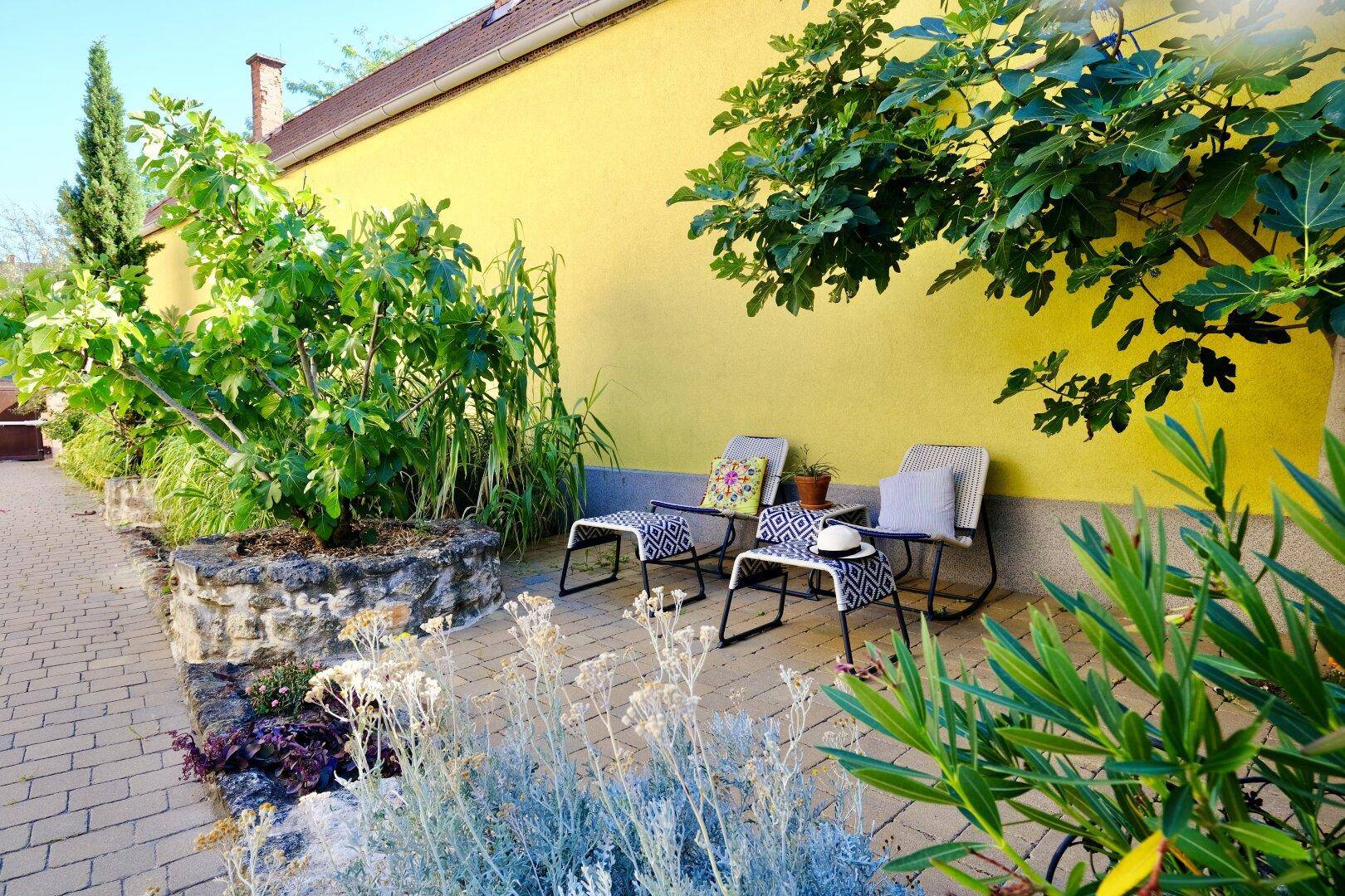 Gemütlicher Sitzbereich im Freien an einer gelben Hauswand mit üppiger Bepflanzung.