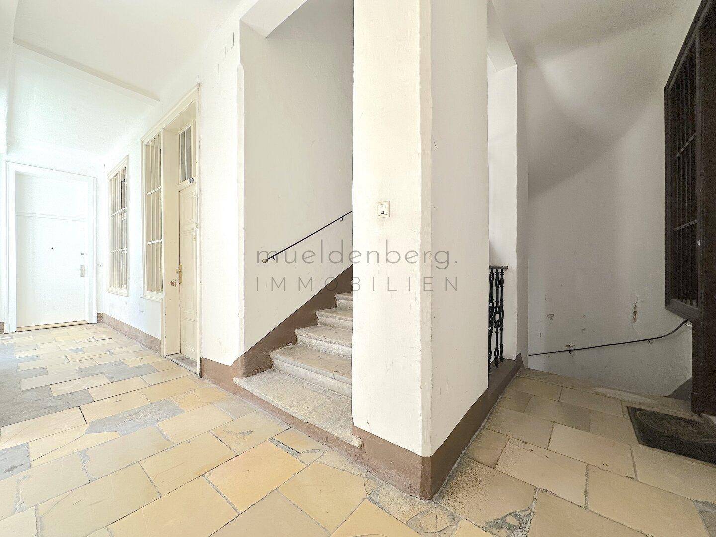 Heller Eingangsbereich mit Steinfliesenboden und einer Treppe, die in die oberen Stockwerke führt.