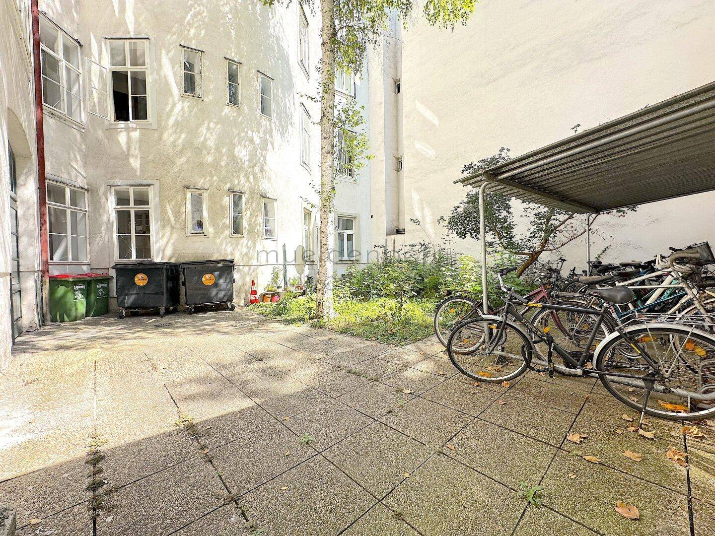 Innenhof mit Fahrradabstellplatz und Mülltonnen, umgeben von Gebäudefassaden.