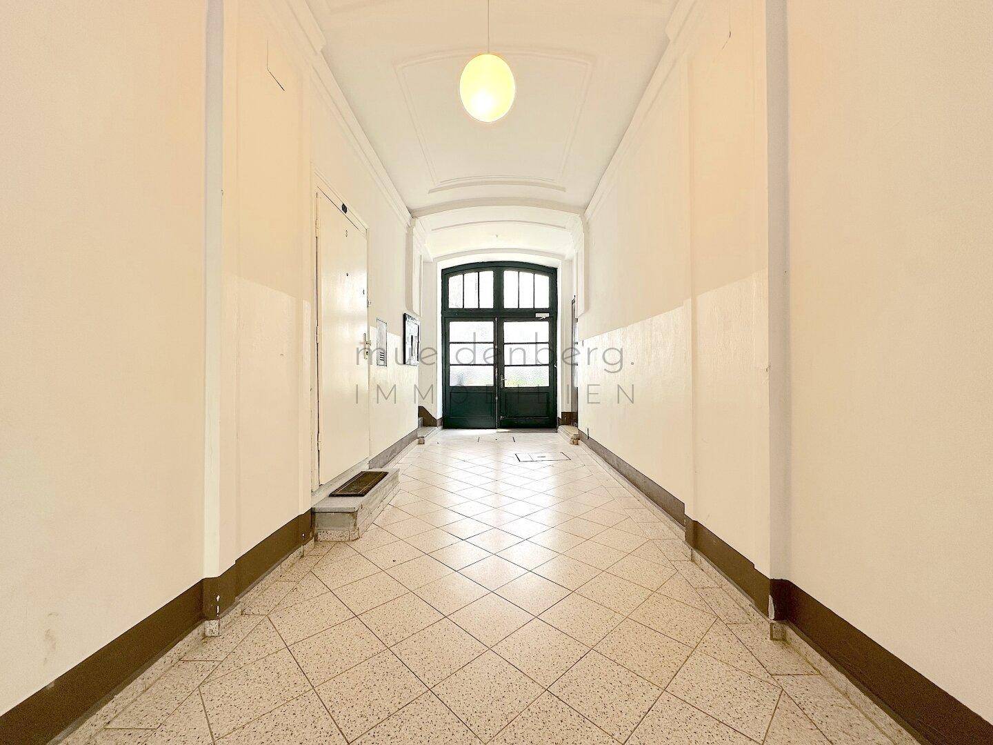 Langer, heller Hausflur mit Fliesenboden und hoher Decke, der zum Eingangsbereich führt.