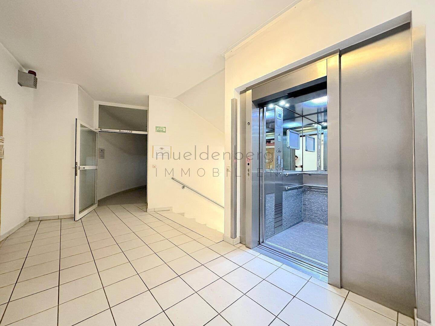 Nahaufnahme des modernen Aufzugs im Treppenhaus, mit offener Kabine und glänzenden Metalltüren.