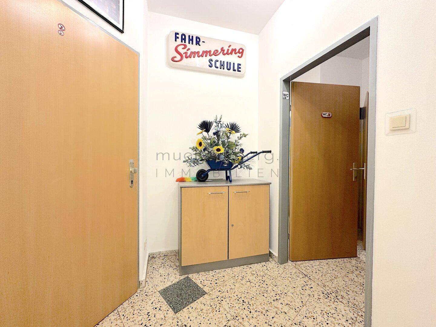 Eingangsbereich mit Terrazzoboden, einem kleinen Schrank und einem dekorativen Schild an der Wand.