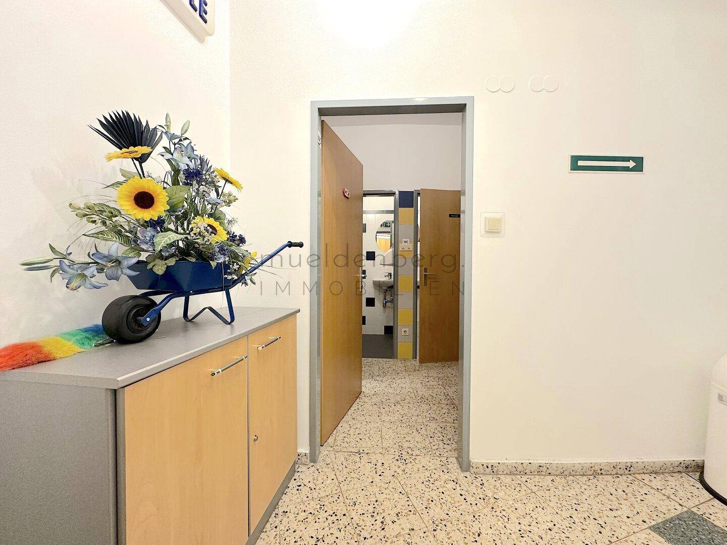 Flur mit Terrazzoboden und einem offenen Durchgang, der zu weiteren Räumen oder Toiletten führt.