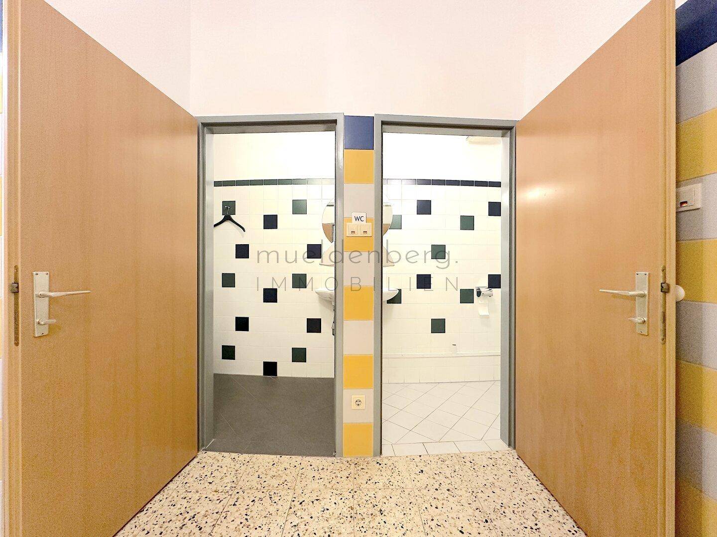 Offene Türen zu den Toiletten, die farbenfrohe Fliesen und einfache Sanitäranlagen zeigen.