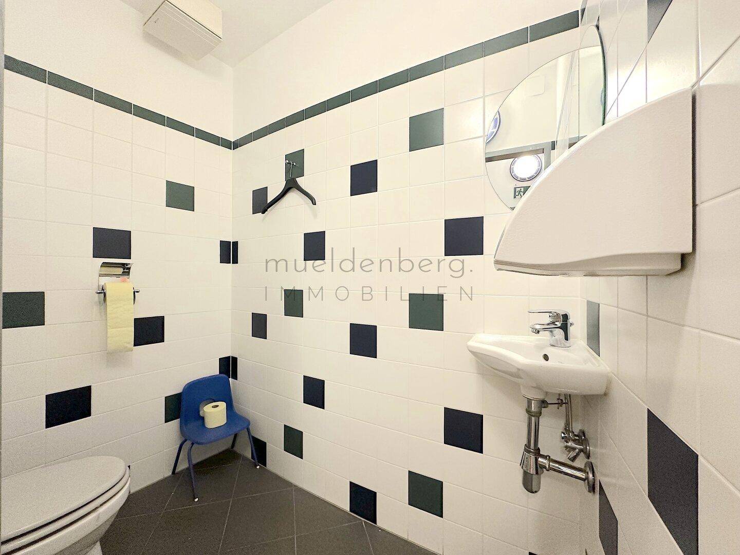 Toilettenraum mit weiß-dunkelgrün gefliesten Wänden, einem Waschbecken und einer Toilette.