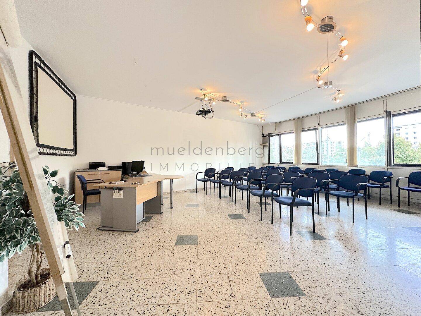 Konferenzraum mit Reihen von blauen Stühlen, einem Projektor und einer Leinwand, ideal für Präsentationen.
