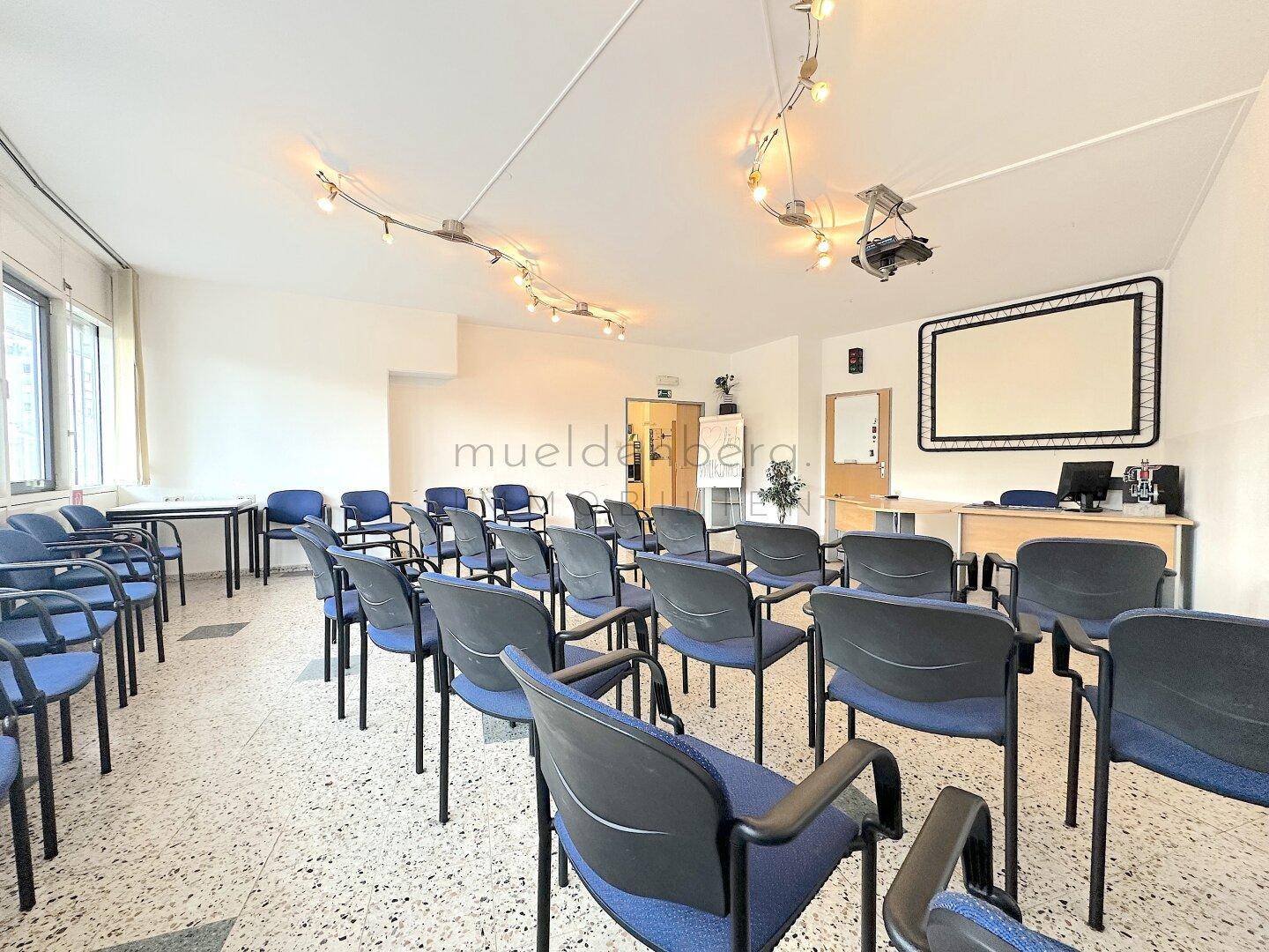 Geräumiger Konferenzraum mit blauen Stühlen in Reihen, ideal für größere Versammlungen und Schulungen.
