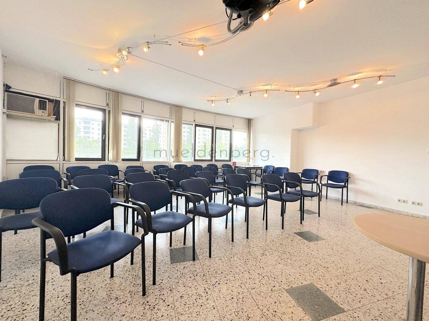 Konferenzraum mit blauen Stühlen, großen Fenstern und einem Projektor, der eine professionelle Umgebung schafft.