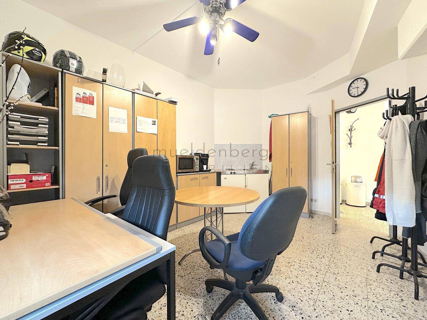 Blick in das Büro mit Schreibtisch, Stauraum und Zugang zu einem Nebenraum, ausgestattet mit praktischen Möbeln.