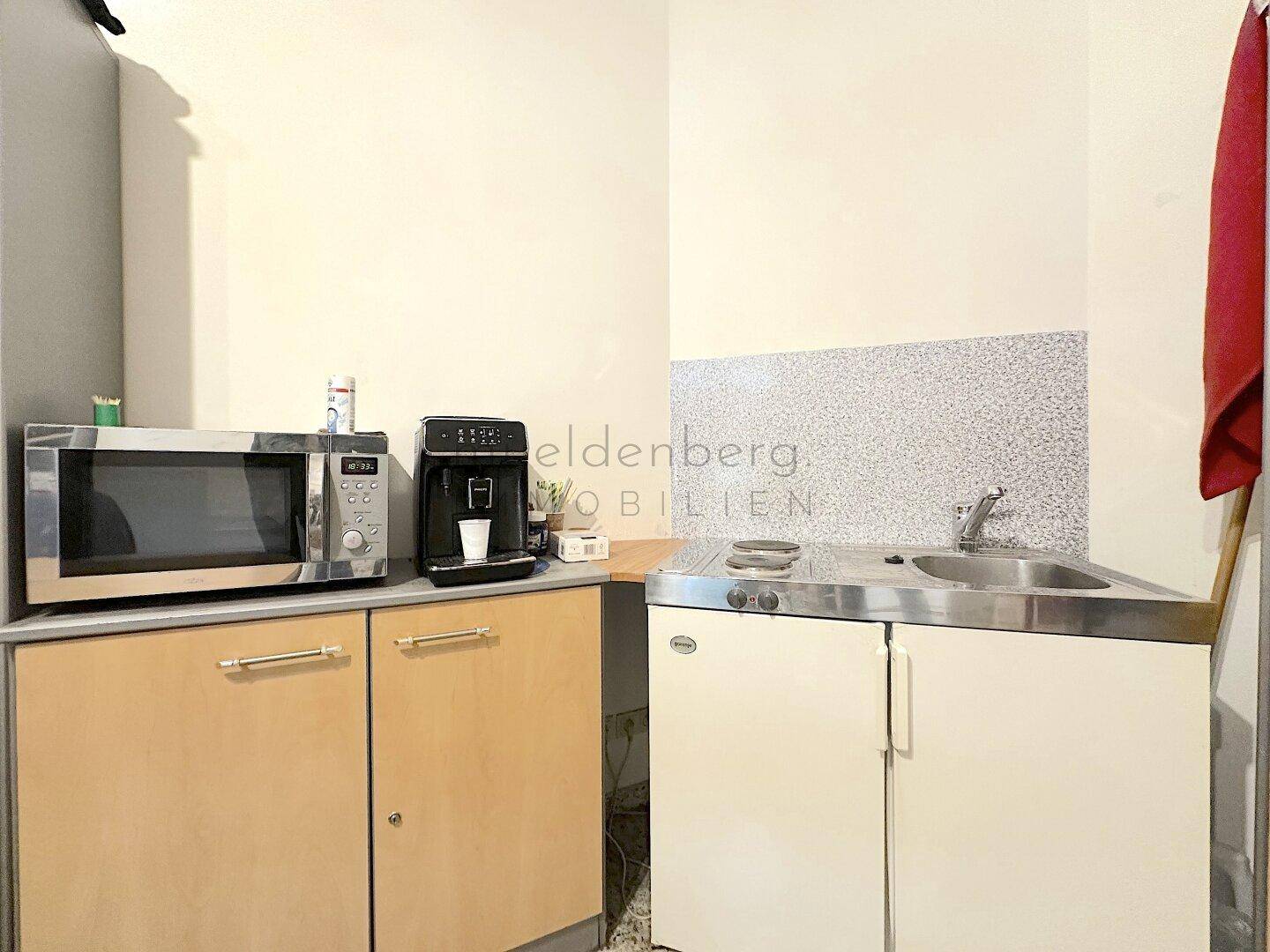 Detailansicht der kompakten Küchenzeile mit Mikrowelle, Kaffeemaschine und Spüle, praktisch für kleine Büros.