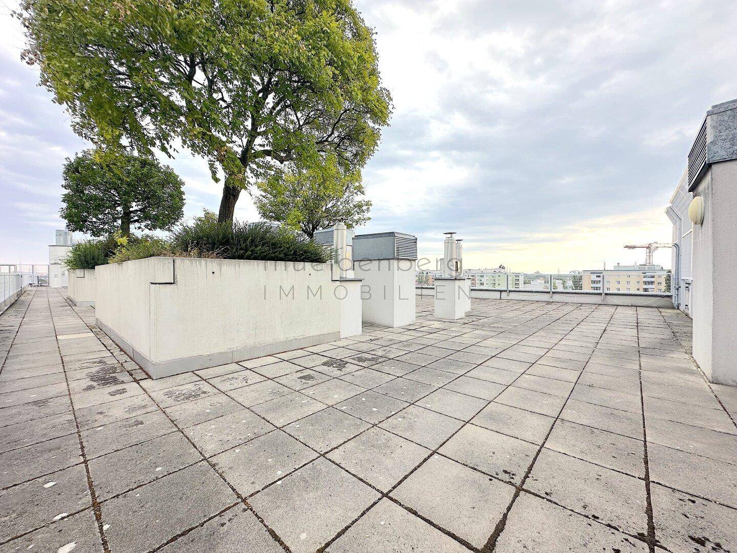 Weitläufige Dachterrasse mit Fliesenboden und Blick auf die Stadtlandschaft in der Ferne, ideal zum Entspannen.