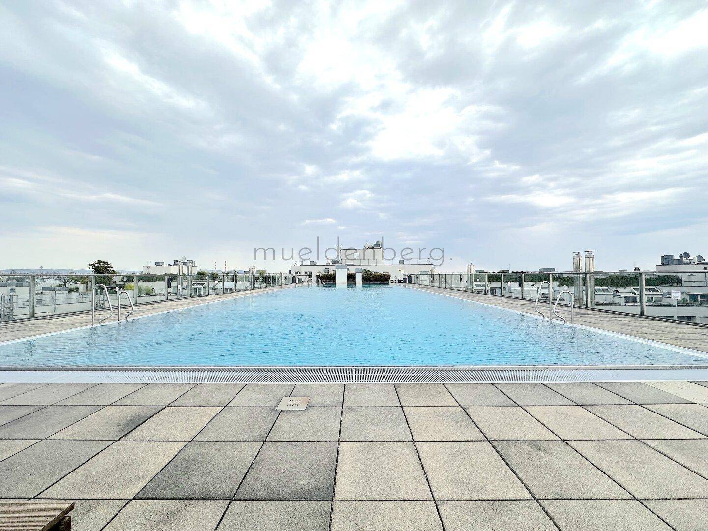 Langer Dachpool mit klarem Wasser und gefliestem Bereich, bietet eine weite Aussicht auf die Stadt.