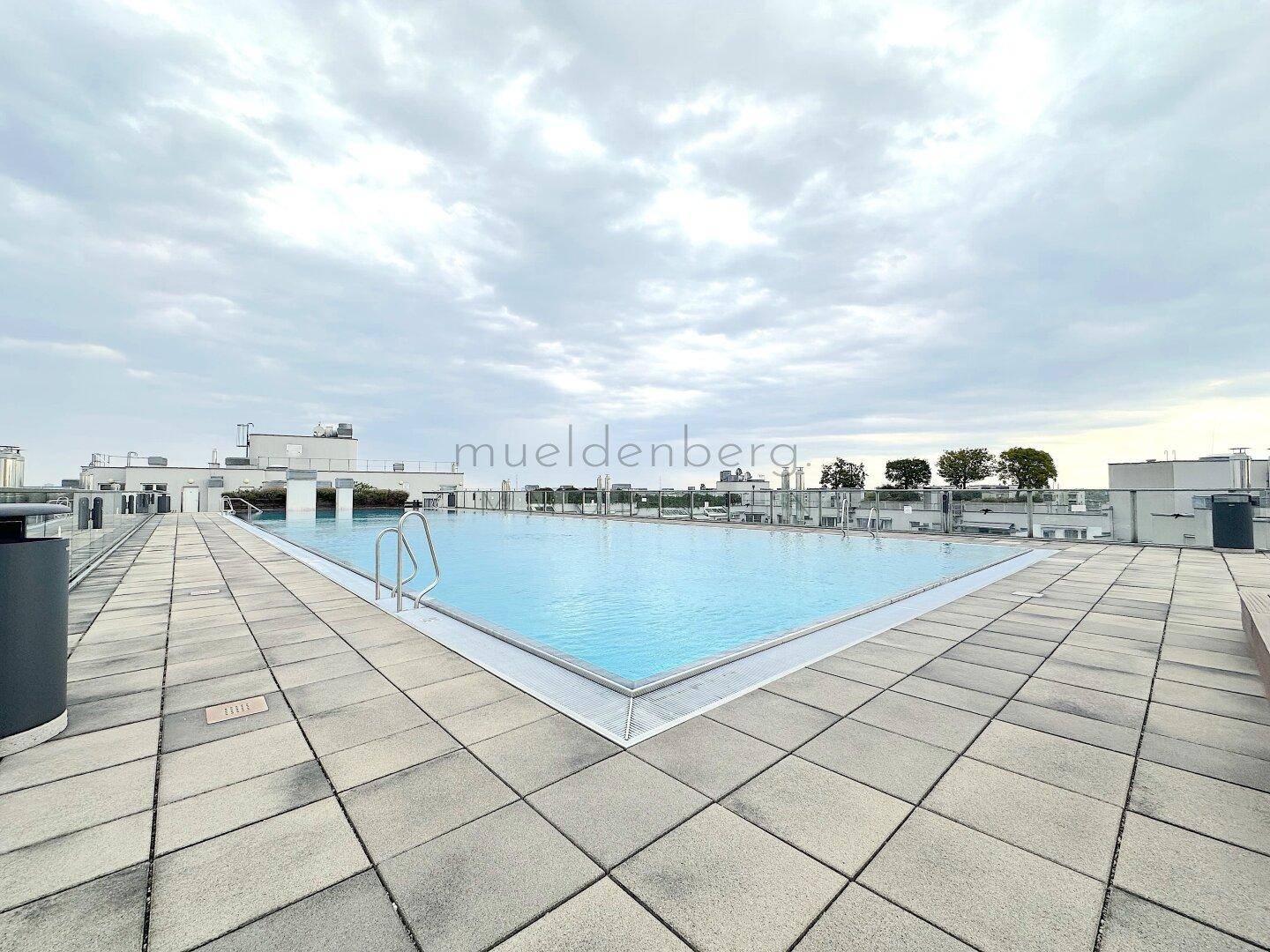 Dachpool mit umlaufenden Fliesen und Blick auf die städtische Umgebung unter einem bedeckten Himmel.