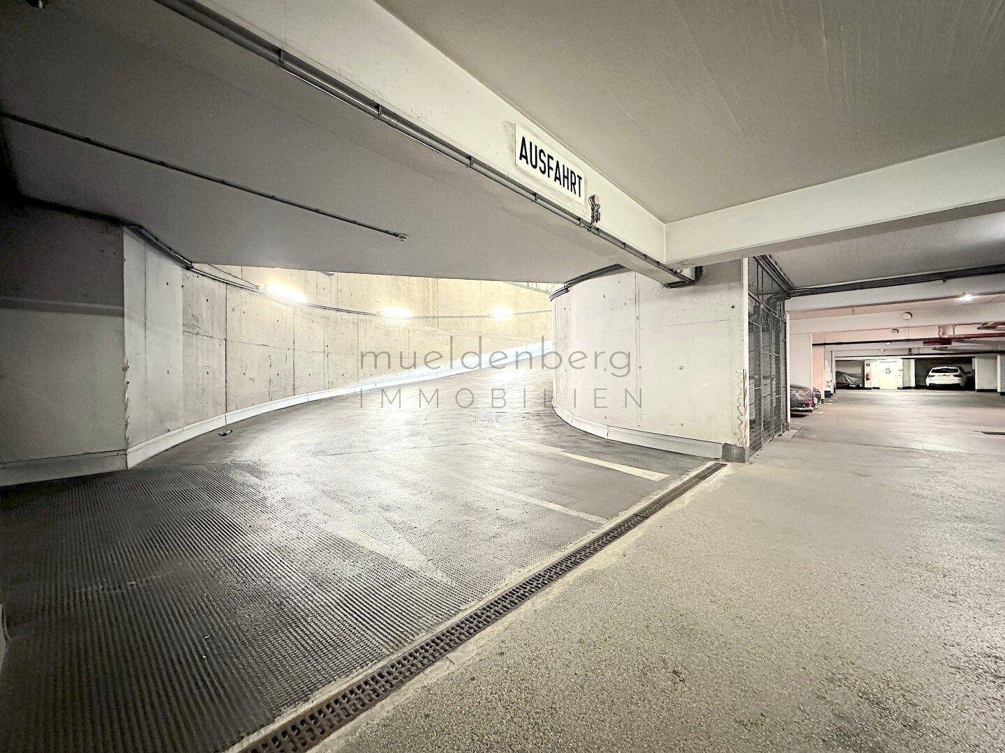 Kurviger Abschnitt der Tiefgarage mit Ausfahrtsschild, Betonwänden und markierten Fahrspuren.