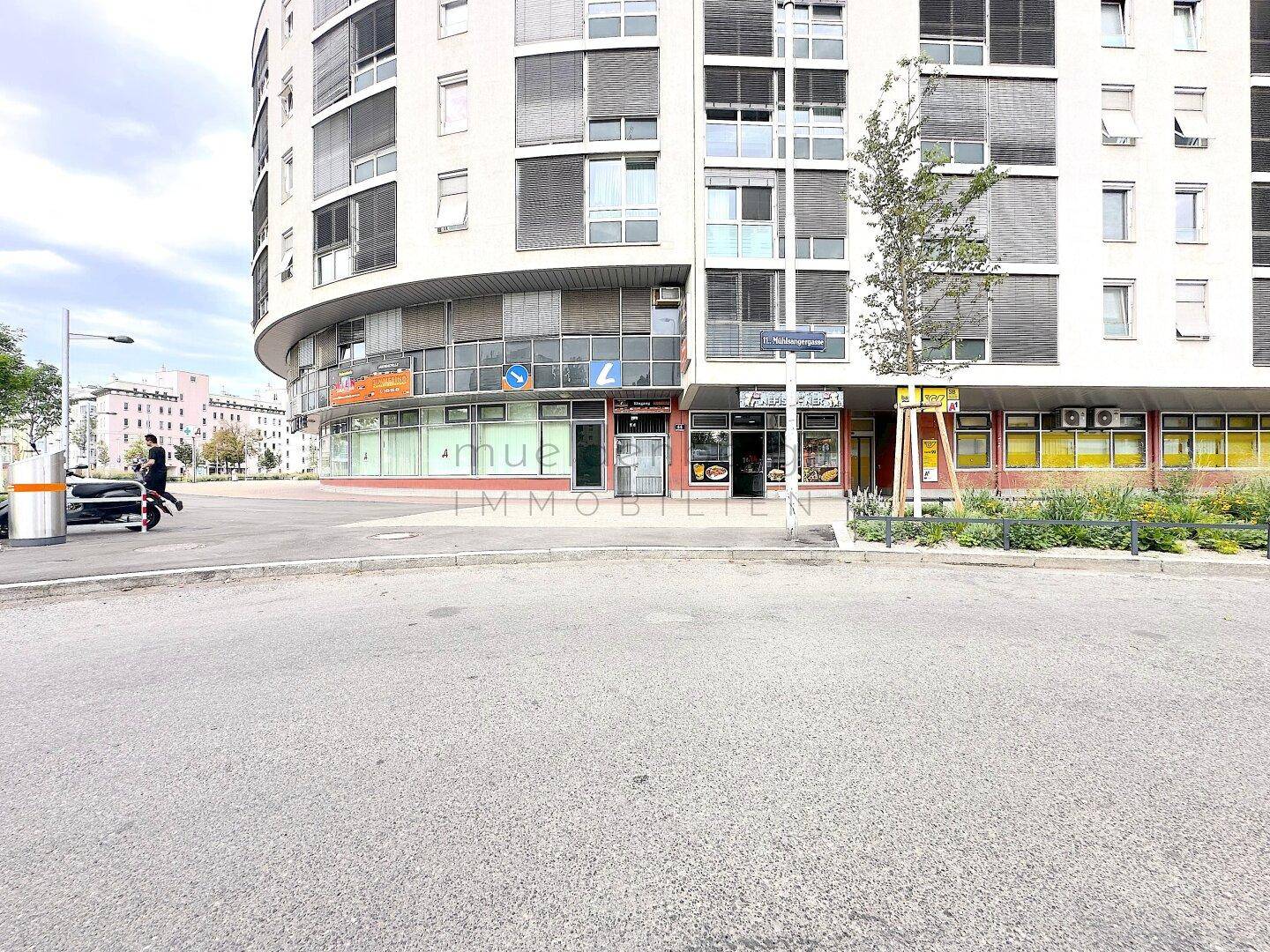 Straßenansicht des Erdgeschosses mit verschiedenen Geschäftseingängen und der modernen Fassade des Gebäudes.