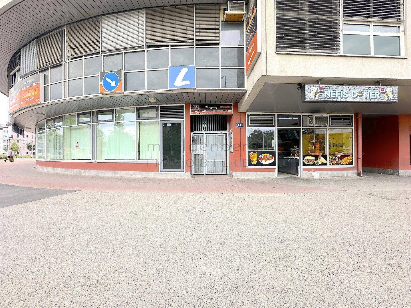 Außenansicht eines Geschäftsgebäudes mit geschwungener Fassade und verschiedenen Ladenfronten, darunter ein Döner-Restaurant.
