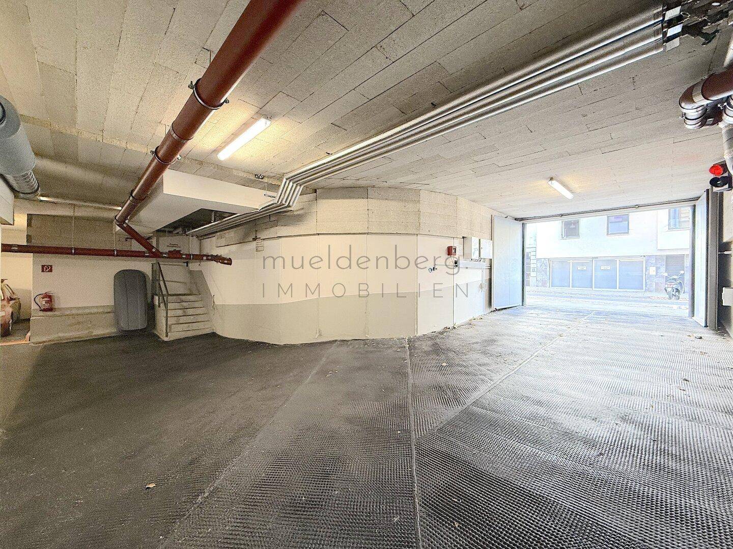 Geräumige Tiefgarage mit Betonstruktur, sichtbaren Rohren und Treppenzugang.
