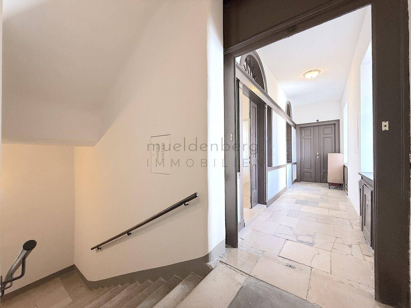 Historischer Flur mit Steinfliesenboden, Holzvertäfelungen und Treppenaufgang im Altbau.