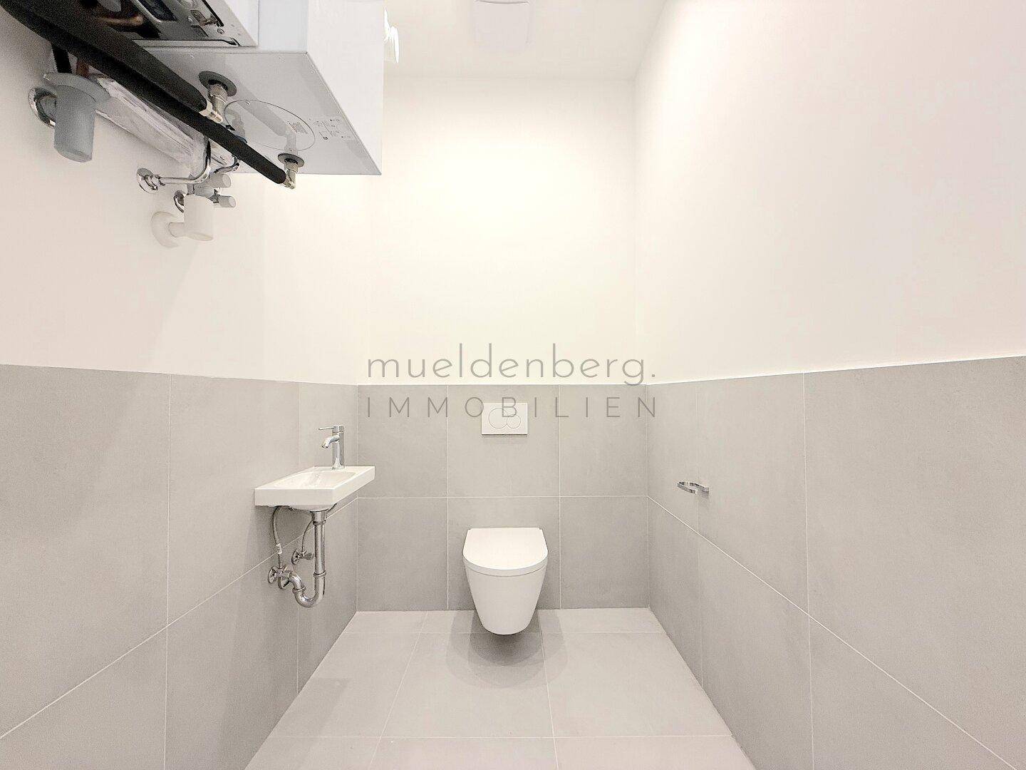Modernes Gäste-WC mit wandhängendem WC, kleinem Waschbecken und grauen Fliesen.
