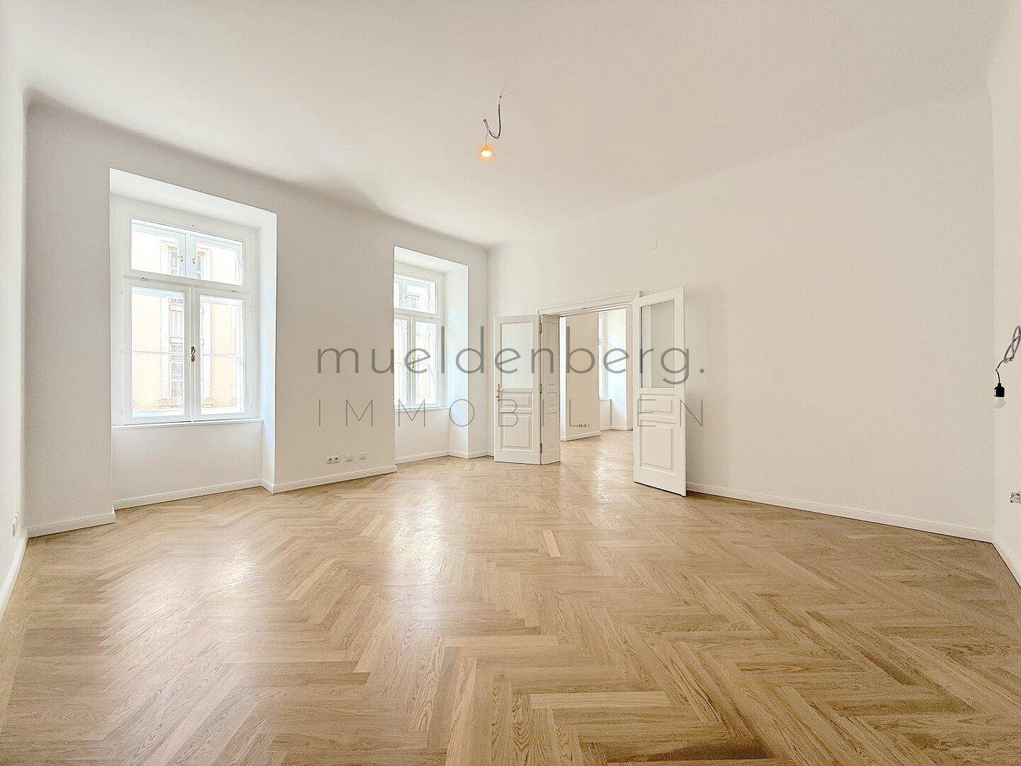 Lichtdurchflutetes Zimmer mit Fischgrätparkett und hohen Decken.