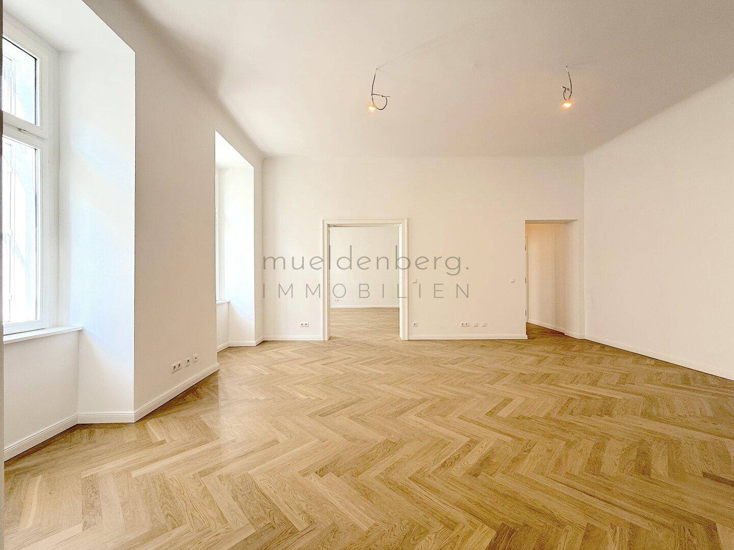 Geräumiger, heller Raum mit Fischgrätparkett und hohen Decken, der mehrere Zugänge bietet.