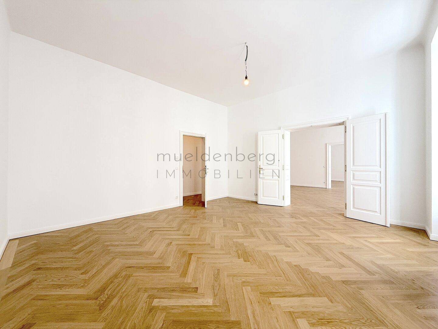 Weitläufiges Zimmer mit Fischgrätparkett und mehreren Türöffnungen, bietet flexible Nutzungsmöglichkeiten.