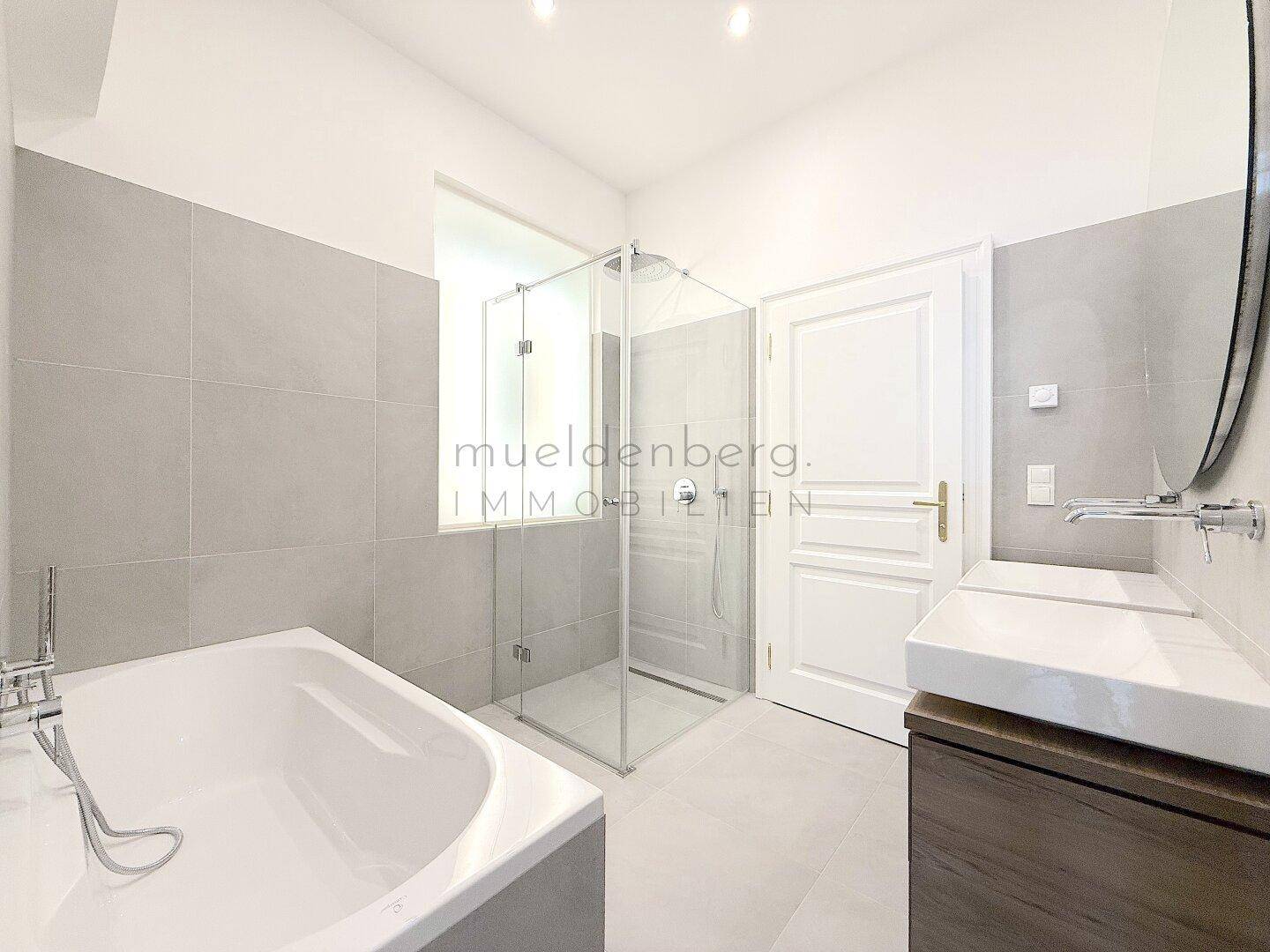 Elegantes Badezimmer mit Badewanne, großer Dusche und modernem Waschtisch, hell gefliest.